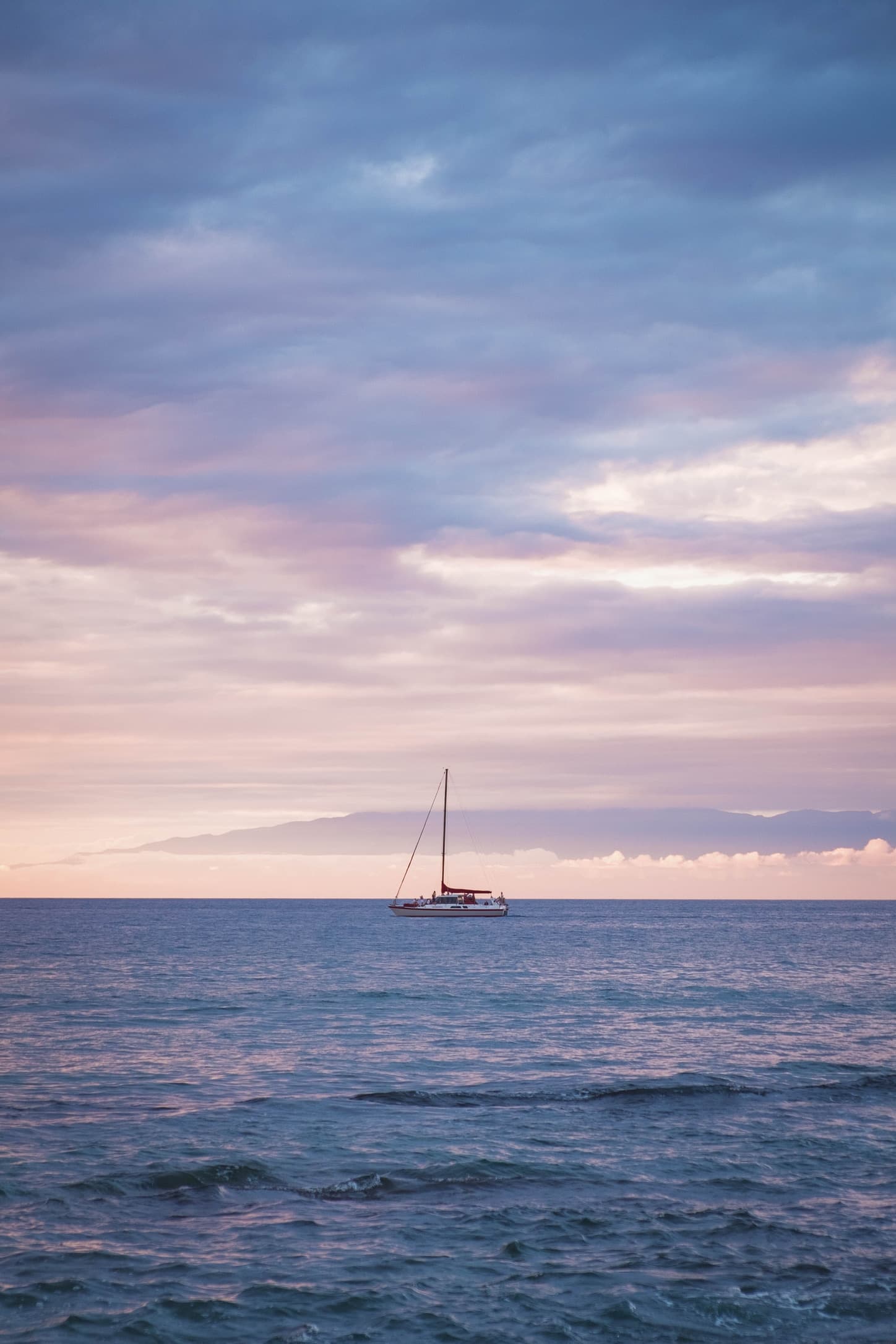 A sailboat on calm water under a pastel sky